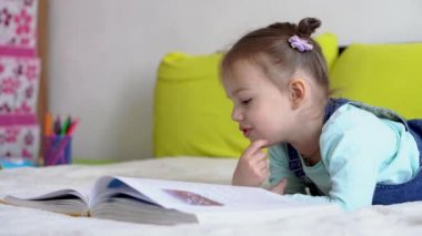 Arkadaşlık, aile, eğitim, akıllı, gülümseyen bir okul çocuğu, küçük kız sarı yatakta büyük, ilginç masallar okuyor. Küçük sevimli okuyucu evde karantinada eğleniyor, mutlu çocuk.