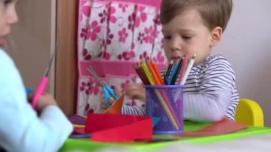 Çevrimiçi öğrenim sanatı eğitimi - İki gülümseyen yaratıcı okul çocuğu sarı yatakta makasla renkli kağıt kesiyorlar. Kardeş küçük ikizler evde karantinada mutlu çocuklar.