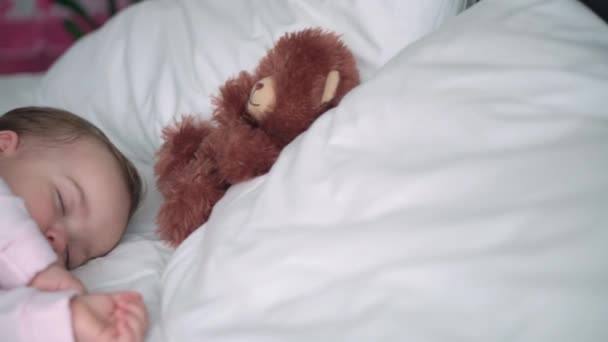 Authentisches Porträt niedlichen kaukasischen kleinen Säugling pummelig Baby Mädchen oder Junge im rosa Schlaf mit Teddybär auf weißem Bett. Mittags ruhen die Kinder. Pflege, Schlafkind, Kindheit, Elternschaft, Lebenskonzept — Stockvideo