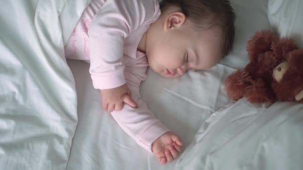 Auténtico retrato lindo bebé caucásico regordete niña o niño en sueño rosa con oso de peluche en la cama blanca. niño descansando a la hora del almuerzo. cuidado, Niñez durmiente, Infancia, paternidad, concepto de vida — Vídeo de stock