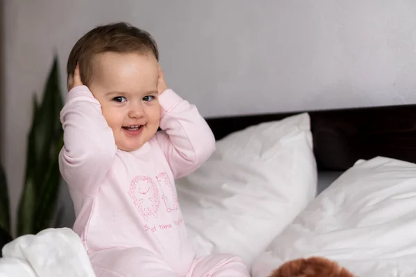 Retrato autêntico caucasiano pequeno bebê gordinha menina ou menino em rosa sonolento ao acordar olhando para a câmera sorrindo bonito e caretas na cama branca. Cuidados infantis, Infância, Paternidade, conceito de vida — Fotografia de Stock