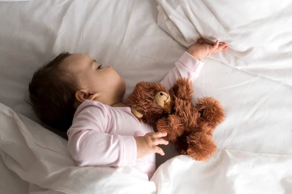 Autentický portrét roztomilý kavkazský malý baculatý holčička nebo chlapec v růžovém spánku s medvídkem na bílé posteli. dítě odpočívající v poledne. péče, Spící dítě, Dětství, Rodičovství, životní koncept — Stock fotografie