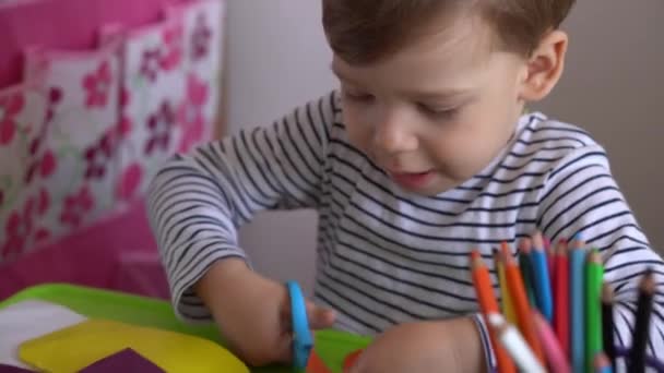 网上学习艺术教育- -一个有创意的幼儿早熟男孩在桌上用剪刀剪出彩色纸。小宝宝快乐的孩子在家里被隔离，手忙脚乱 — 图库视频影像
