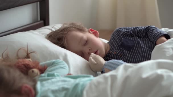 本物の肖像画かわいい白人の小さな就学前の兄弟赤ちゃんの男の子と白いベッドの上でテディベアと青の睡眠中の女の子。お昼休みの子。ケア、医療、健康、子供時代、人生の概念 — ストック動画