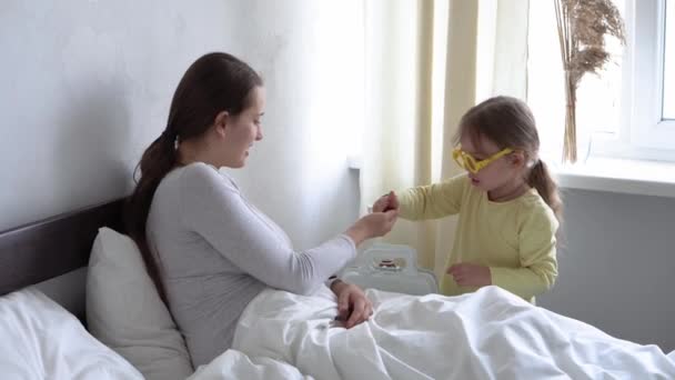 Lindo bebé niña médico o enfermera con mamá enferma o niñera en el dormitorio da pastillas. cuidar de pasar tiempo libre de la familia en casa juntos, juego de rol. Maternidad, medicina y concepto de salud — Vídeos de Stock