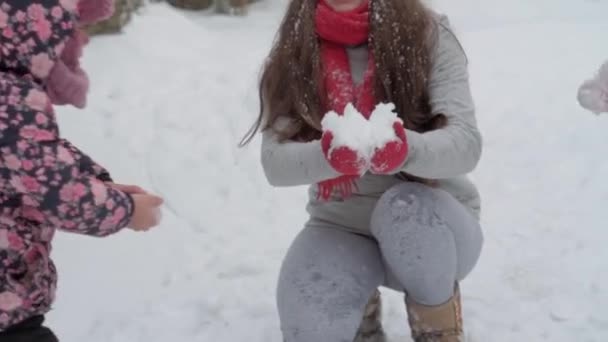 Slo-mo authentieke schattige jonge vrouw moeder met rode hoed met kinderen sneeuw nemen met de handen overgeven hoofd glimlach. sneeuwval in het winterpark buiten. moederschap, moederdag, vakantie, familieconcept — Stockvideo