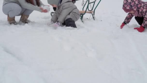 Urlaub, Spiel, Familienkonzept - slo-mo authentische 3 glückliche Vorschulkinder Geschwister mit jungen wonan Mutter vieler Kinder schaufeln Schnee. Schneefall in der kalten Jahreszeit im Wintergarten im Freien — Stockvideo