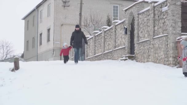 Yavaş çekim otantik mutlu genç adam siyahlı baba ve küçük oğlu karlı yolda eziliyorlar. Soğuk mevsimde kar yağışı açık havada kış parkında olur. Babalık, Babalar Günü, Ebeveynlik, Aile, Hayat Konsepti — Stok video