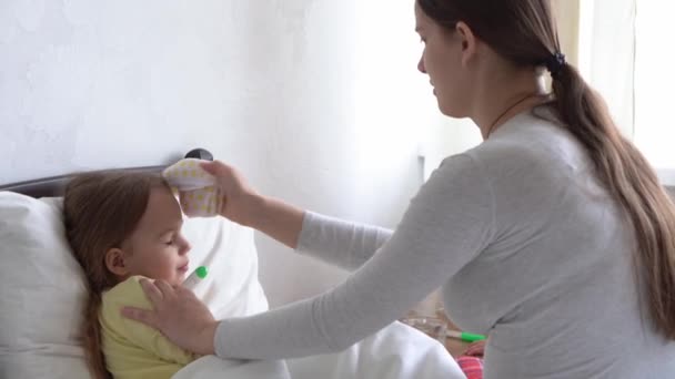 Giovane donna caucasica infermiera o medico esamina neonata misura la temperatura con termometro sotto braccio sul letto bianco. Mamma si prende cura del bambino malato. medicina e salute, maternità, concetto covid-19 — Video Stock