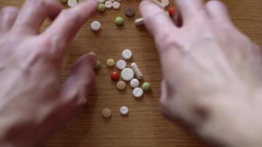 Erkek tokalaşan parmaklar ahşap masaya saçılmış renkli haplar alıyor. Hasta adam korku içinde tedavi arıyor. Geleneksel ve Alternatif Tıp ve Sağlık, covid-19 kavramı