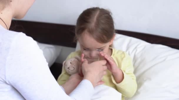 Zblízka mladý běloška žena zdravotní sestra nebo lékař pediatr zkoumá dítě dívka dát pít sklenici vody na bílé posteli. Máma se stará o nemocné dítě. medicína a zdraví, mateřství, koncept covid-19 — Stock video