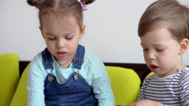 Apprentissage en ligne éducation artistique - Deux souriants créatifs préscolaire, tout-petits enfants font artisanat découper du papier coloré avec des ciseaux sur lit jaune. Frères et sœurs petits jumeaux enfants heureux en quarantaine à la maison — Video