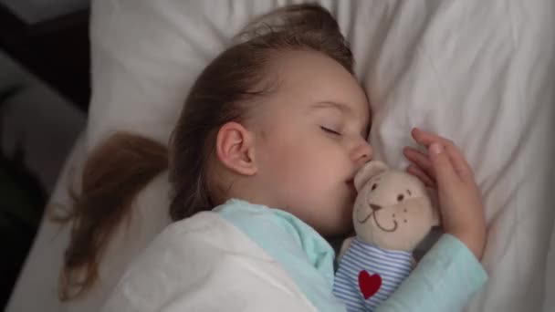 Autentický portrét nemocné roztomilé kavkazské dítě předškolní Dívka v modrém spánku s plyšovým medvídkem na bílé posteli. dítě odpočívající v poledne. péče, medicína a zdraví, Dětství, Rodičovství, životní koncept — Stock video