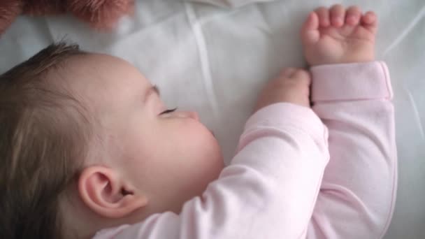 확실 한 초상화귀여운 코카서스의 작은 아기가 분홍색 침대에 테디베어 와 함께 잠을 자고 있거나 남자 아이가 흰색 침대에 누워 있다. 아이는 점심 시간에 쉬고 있습니다. 보육, 잠자는 아이, 어린 시절, 부모로서의 삶의 개념 — 비디오