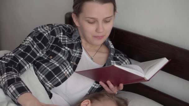 Authentique jeune femme mignonne ou baby-sitter lit conte de fées du livre aux enfants avant le coucher. Maman s'occupe des enfants endormis. Deux bébés dormant dans un lit blanc. Fête des mères, maternité, enfance — Video