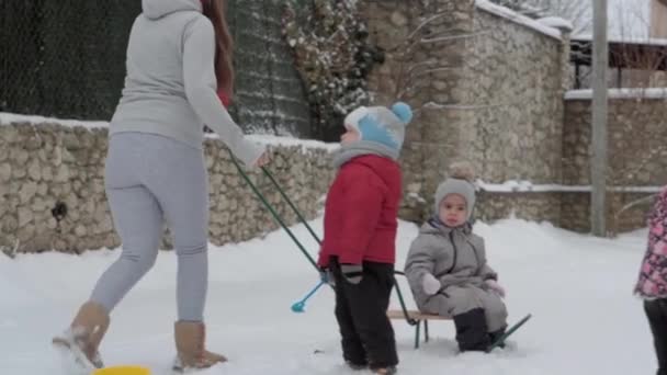 Vacation, game, family concept - slo-mo authentic three happy preschool toddler kids siblings with young wonan mom sledding and play with snow. snowfall in cold season weather in winter yard outdoors — Stock Video