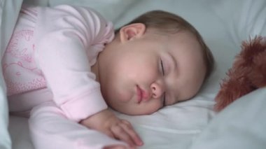 Otantik portre, beyaz yatakta oyuncak ayıyla pembe uykuda olan beyaz, beyaz, küçük, beyaz, tombul bir bebek bebek ya da oğlan. Çocuk öğle yemeği vakti dinleniyor. Bakım, Uyuyan Çocuk, Çocukluk, Ebeveynlik, Hayat Konsepti