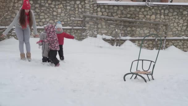 子供たちと一緒に喜んで蒸留笑顔で雪の中を走ると赤い帽子の子供たちとslo-mo本物のかわいい幸せな若い女性のお母さん。冬の屋外での降雪。母親の日休暇家族の概念 — ストック動画