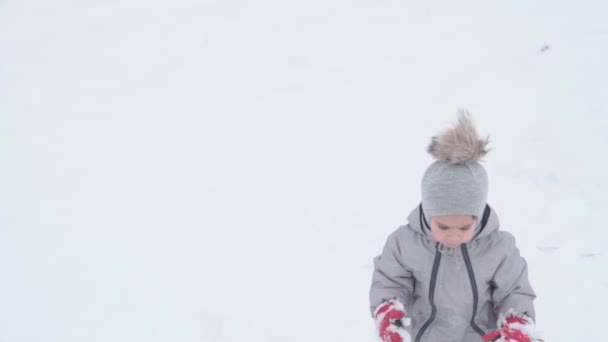 Férias, jogo, conceito de infância - slo-mo autêntica criança pré-escolar oriental feliz bebê sorrir olhando para a câmera e tentando andar na neve profunda. queda de neve na estação fria tempo no inverno ao ar livre — Vídeo de Stock