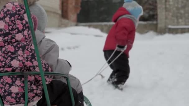 Vacanza, gioco, concetto di famiglia - Slo-mo autentico tre felici bambini in età prescolare fratelli con la giovane mamma wonan slittino e giocare con la neve. nevicate in stagione fredda tempo in cortile invernale all'aperto — Video Stock