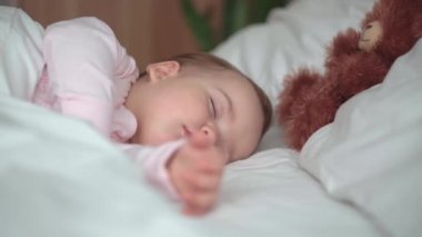 Otantik portre, beyaz yatakta oyuncak ayıyla pembe uykuda olan beyaz, beyaz, küçük, beyaz, tombul bir bebek bebek ya da oğlan. Çocuk öğle yemeği vakti dinleniyor. Bakım, Uyuyan Çocuk, Çocukluk, Ebeveynlik, Hayat Konsepti