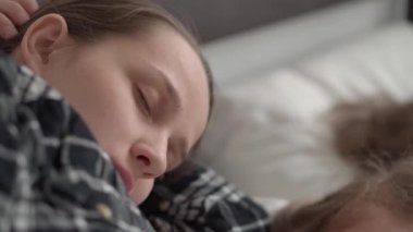 Genç, otantik anne uyuya kaldı yatmadan önce kitaptan bebeğe masal okudu. Kadın uyuyan çocuklara bakıyor. Beyaz yatakta uyuyan iki çocuk. Anneler günü, annelik, çocukluk kavramı.