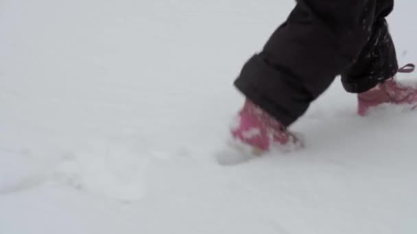 Winter, Urlaub, Spiel, Familienkonzept - Zeitlupe hautnah Babyspaziergang durch tiefen Schnee. Kinderfüße treten auf verschneiten Pfaden. Vorschulkind in schwarzem Overall bei Schneefall in der kalten Jahreszeit — Stockvideo