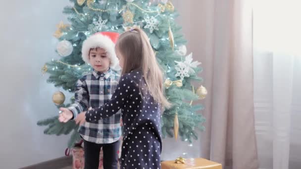 2 niños felices auténticos de la alegría alrededor de la danza cogidos de la mano caminan en círculo por el juego del árbol de Navidad se divierten juntos. Los niños preescolares celebran el ambiente festivo de Año Nuevo. Invierno, concepto de vacaciones — Vídeo de stock