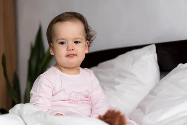 Hiteles portré kaukázusi kis csecsemő pufók kislány vagy fiú rózsaszín álmos ébredéskor nézett kamera mosolyog aranyos és grimasz fehér ágyban. Gyermekgondozás, Gyermekkor, Szülőség, életkoncepció — Stock Fotó
