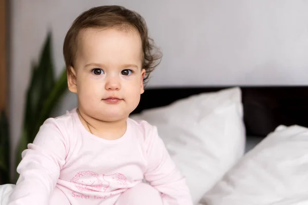 Authentique portrait mignon caucasien petit bébé joufflu bébé fille ou garçon en somnolence rose au réveil en regardant la caméra dans un lit blanc. garde d'enfants, enfance, parentalité, concept de style de vie — Photo