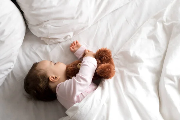 Äkta porträtt söt kaukasiskt litet spädbarn knubbig liten flicka eller pojke i rosa sömn med nalle på vit säng. Barnet vilar vid lunchtid. vård, Sömnunge, Barndom, Föräldraskap, livskoncept — Stockfoto