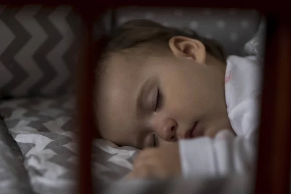 Söt glad liten knubbig liten flicka sover sött i grå babysäng under lunchrasten i vit och rosa pyjamas med nalle hemma. Barndom, fritid, komfort, medicin, hälsa koncept — Stockfoto