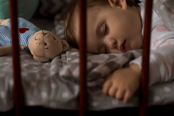 Aranyos vidám kis pufók kislány alszik édesen szürke baba bölcső ebédidő alatt pihenő fehér és rózsaszín pizsamában macival otthon. Gyermekkor, szabadidő, kényelem, orvostudomány, egészség fogalma — Stock Fotó
