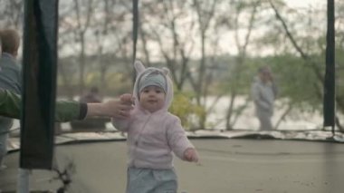 İlkbahar, spor, bayram, aile, çocukluk üç mutlu küçük çocuk anaokulu kardeş çocuklar trambolinde zıplayarak eğleniyorlar güneşli bir akşam günbatımında parkta.