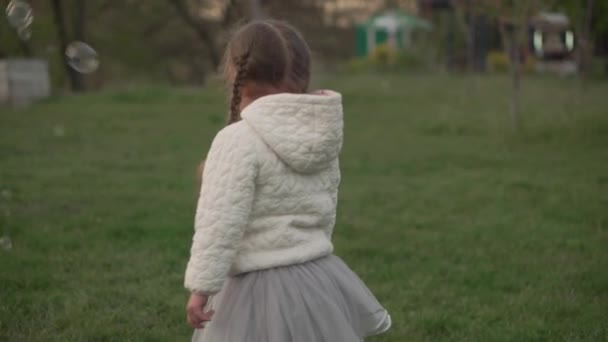 Pequeños hermanos preescolares niños y niñas atrapan burbujas de jabón en el parque de primavera al atardecer. Felices amigos de los niños se divierten pasar tiempo. Tiempo libre naturaleza. Familia, amistad, concepto de infancia — Vídeo de stock