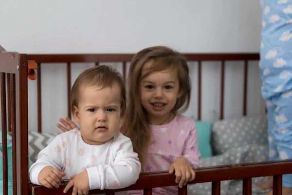 Söt glad 3 små barn flicka och pojke syskon förskola barn i grå babysäng efter att ha vaknat upp ur sömnen i pyjamas med benen dinglande. Barndom, fritid, komfort, medicin, hälsa koncept — Stockfoto