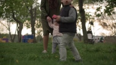 Genç kadın anne, küçük kız bebeğini bahar parkında çimlerde yürümeyi öğreniyor. Mutlu çocuk, ilk adımı at Sunset 'te iyi eğlenceler. Aile Çocukluğu Eğlence Zamanı Doğanın dışında