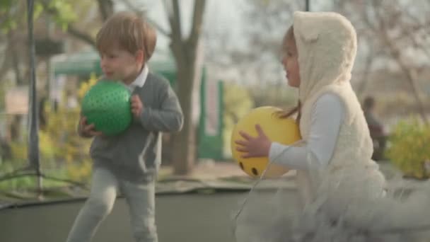 Primavera, deporte, día de fiesta, familia, infancia - cámara lenta Tres hermanos preescolares niños pequeños felices niños gemelos jugar divertirse saltar bolas en trampolín al aire libre soleado atardecer en el parque — Vídeos de Stock