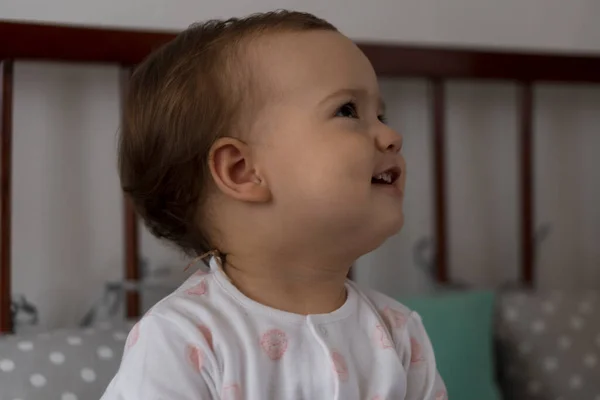 Leuke vrolijke kleine mollige baby meisje zitten in grijze babybedje na het wakker worden in witte en roze pyjama met teddybeer en glimlachen. Jeugd, vrije tijd, comfort, geneeskunde, gezondheidsconcept — Stockfoto