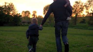 Parktaki insanlar. Gün batımında mutlu aile silueti. Baba ve bebek el ele tutuşarak zaman geçirdiler. Aileler ve eğlenceli çocuklar açık havada yürüyorlar. Babalar Günü, çocukluk, ebeveynlik kavramı.