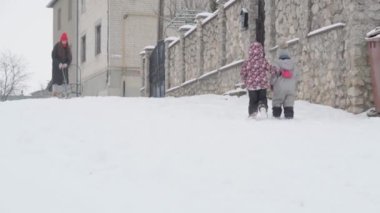 Tatil, oyun, aile kavramı. Ağır çekim otantik. İki yorgun anaokulu çocuğu. Şapkalı ve eldivenli çocuklar birlikte tepeye tırmanıyorlar. Soğuk mevsimde kar yağışı, kış parkında açık havada.