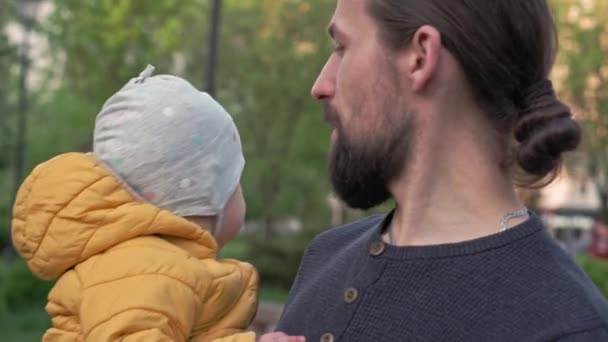 People in park. dad hold baby daughter girl in arms and tickles have spend time. parents and fun children walking outdoors in open air. Fathers day, happy family, childhood, parenthood concept — Stock Video