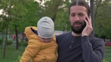 Parktaki insanlar. Baba, kucağında küçük bir kızla telefonda konuşuyor. Aileler ve eğlenceli çocuklar açık havada yürüyorlar. Babalar Günü, mutlu aile, çocukluk, ebeveynlik kavramı.