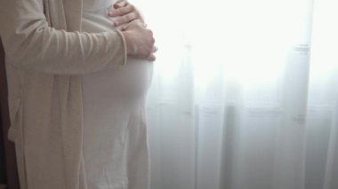 Otantik, tatlı, hamile bir kadın çocuğuna baktığı için kendini mutlu hissediyor. Gencecik bir anne karnında bebeğini pencerenin yanında tutuyor. Doğum öncesi bakım ve hamilelik, annelik, yaşam tarzı konsepti