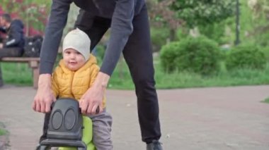 Parktaki insanlar. Baba, küçük kızı motorsiklete bindirip gezdirmiş ve gezdirmiş. Aileler ve eğlenceli çocuklar açık havada yürüyorlar. Babalar Günü, mutlu aile, çocukluk, ebeveynlik kavramı.