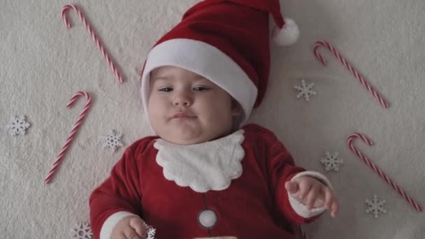 Veselé Vánoce, šťastný nový rok, kojenci, dětství, dovolená koncept - close-up úsměv 7 měsíců legrační novorozenec v Santa Claus klobouk, červená bodysuit hrát na bílé měkké posteli lízat sladké vánoční cukroví