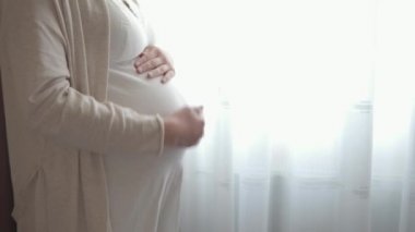 Otantik, tatlı, hamile bir kadın çocuğuna baktığı için kendini mutlu hissediyor. Gencecik bir anne karnında bebeğini pencerenin yanında tutuyor. Doğum öncesi bakım ve hamilelik, annelik, yaşam tarzı konsepti