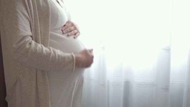 Authentieke schattige zwangere vrouw die zich gelukkig voelt en voor het kind zorgt. Jonge moeder die een baby in de buik bij het raam houdt. Zwangerschap prenatale zorg en zwangerschap, moederschap, levensstijl concept — Stockvideo