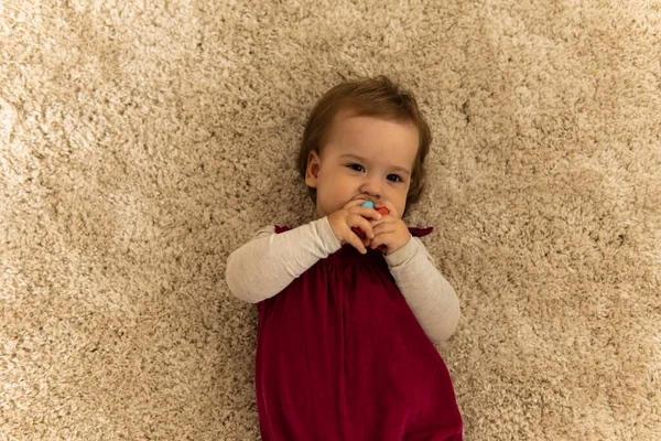 Забота, детство - сверху портрет одного маленького счастливого смешного улыбающегося малыша в розовом с веселыми обнимающимися ногами, лежащими на мягком белом коврике на полу в уютном милом доме — стоковое фото