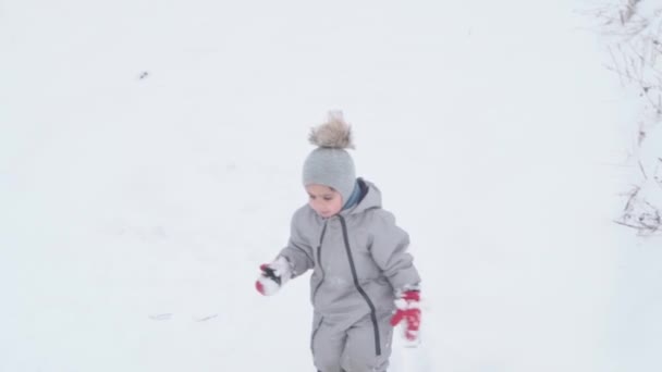 Semester, spel, barndomskoncept - and mo autentisk glad östlig förskola småbarn pojke leende tittar på kameran och försöker gå i djup snö. snöfall i kallt väder på vintern utomhus — Stockvideo